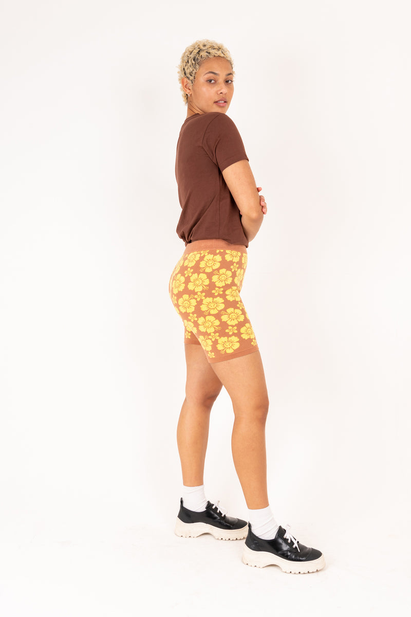 Person wearing a brown t-shirt and yellow floral shorts on a white background