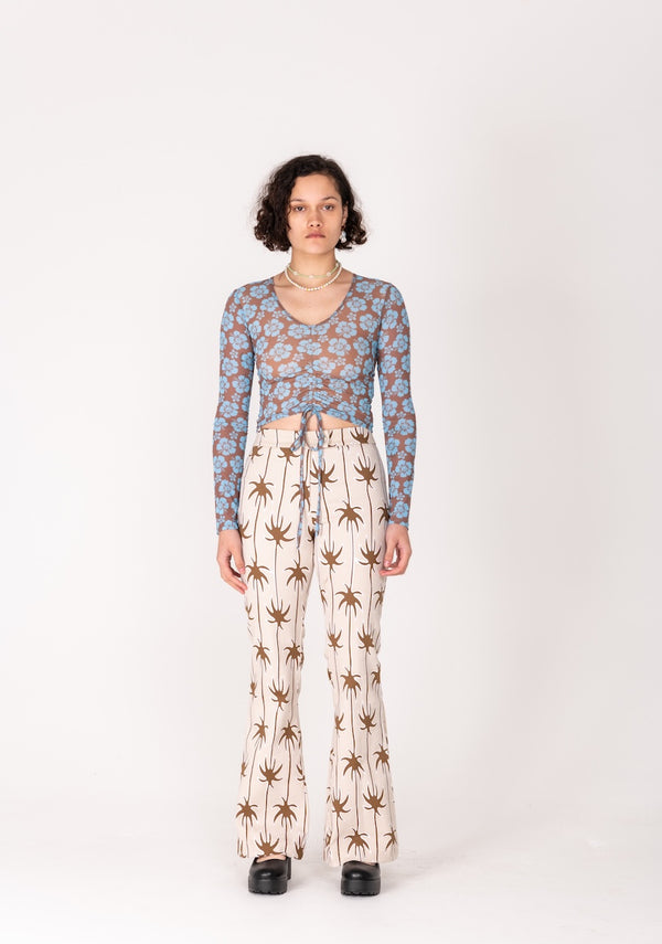 Person wearing a patterned long-sleeve top and palm tree print pants on a white background