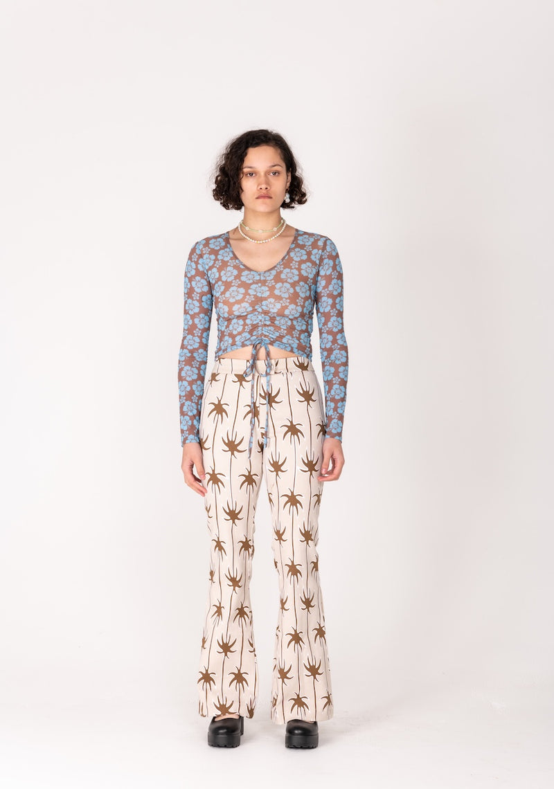 Person wearing a patterned long-sleeve top and palm tree print pants on a white background