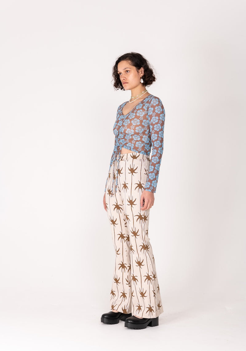 Woman wearing a floral top and palm tree patterned pants on a white background