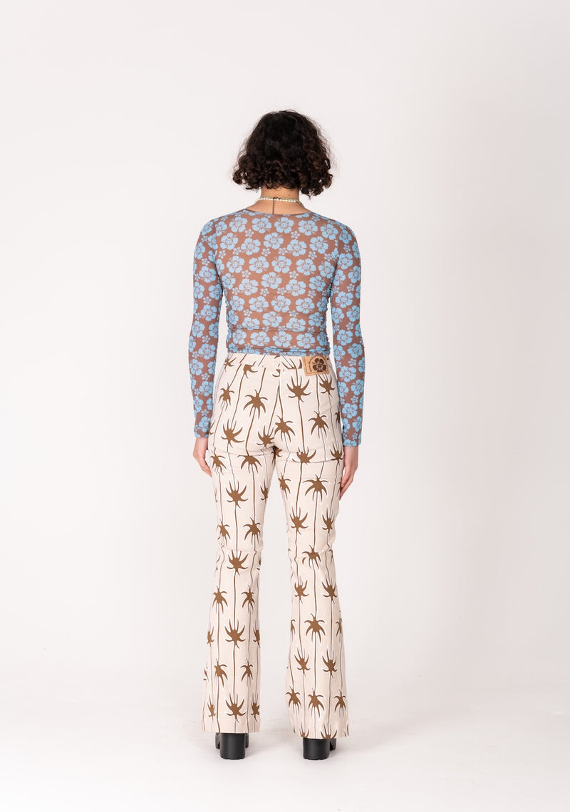 Person wearing a blue floral top and white pants with brown patterns on a white background