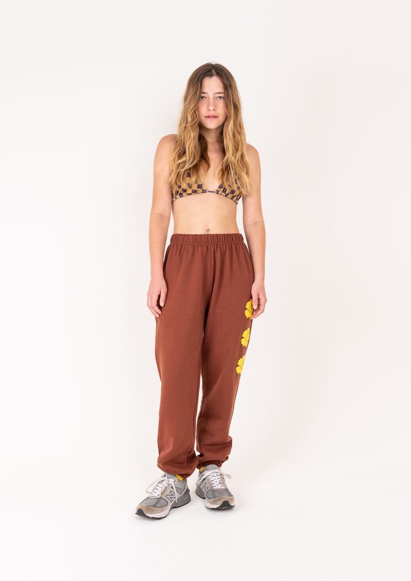Woman wearing brown sweatpants with yellow floral patterns on a white background