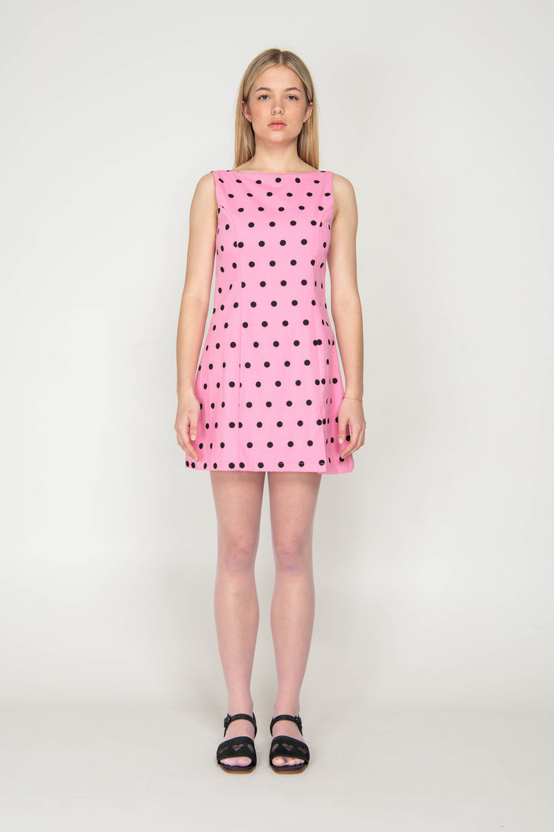 Woman wearing a pink dress with black polka dots on a white background