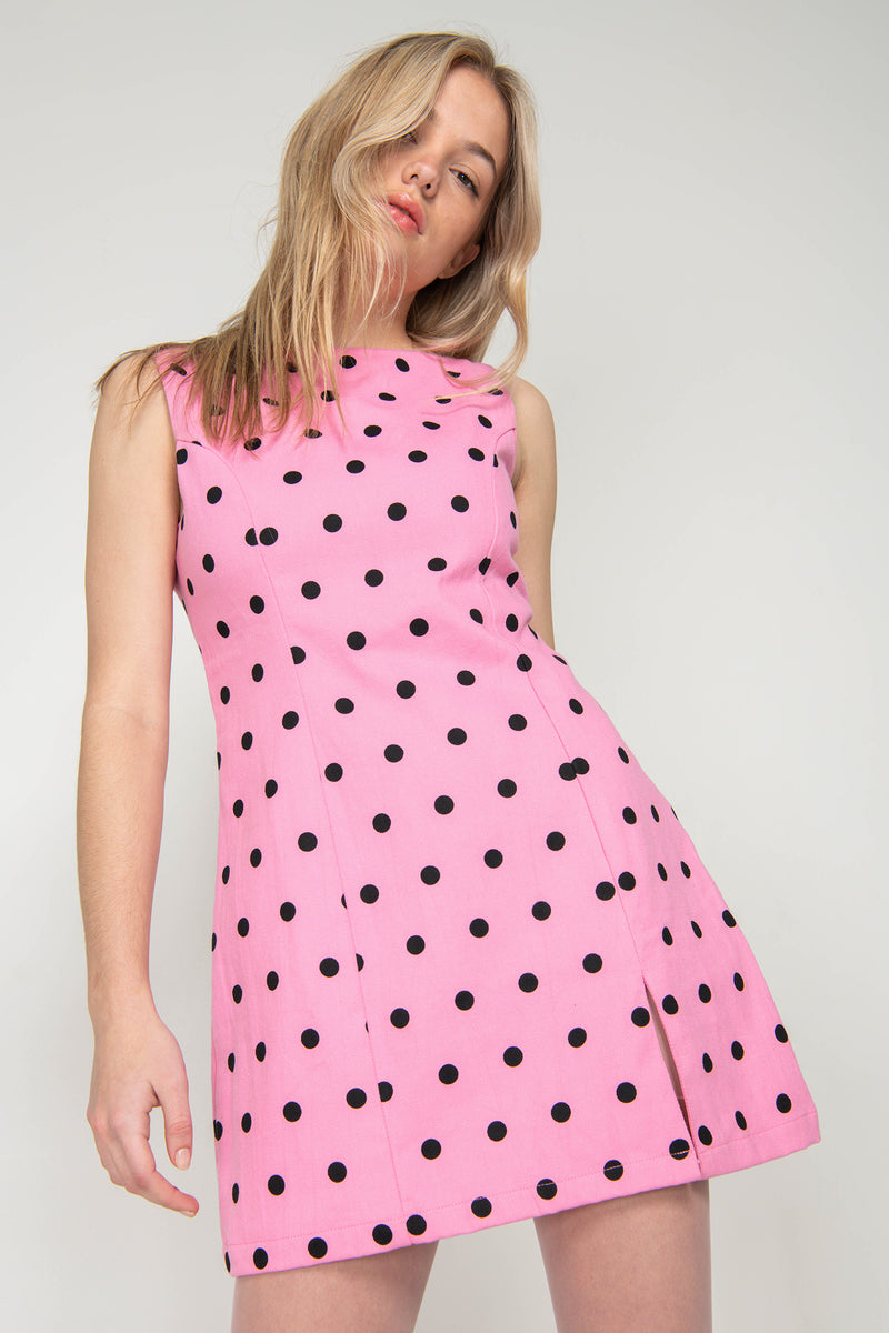 Woman wearing a pink dress with black polka dots on a plain background