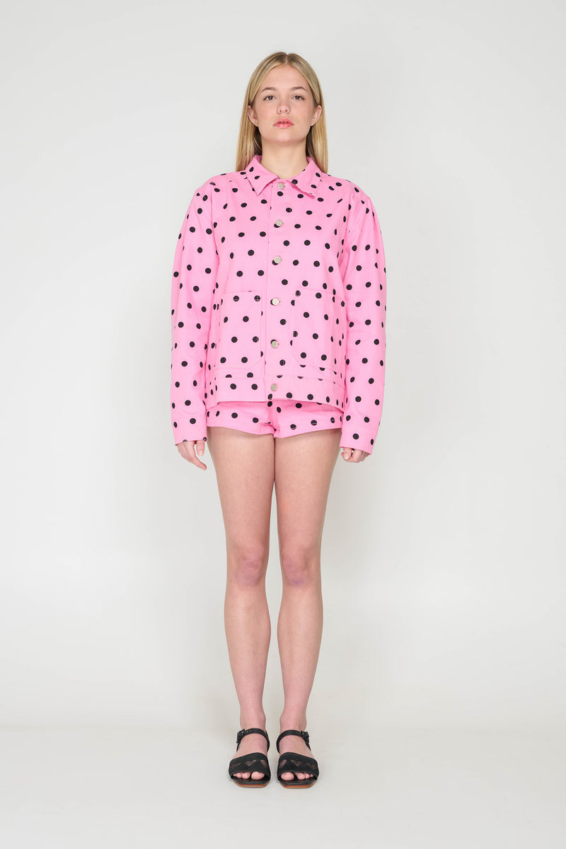 Person wearing a pink hoodie with black polka dots and matching shorts on a white background
