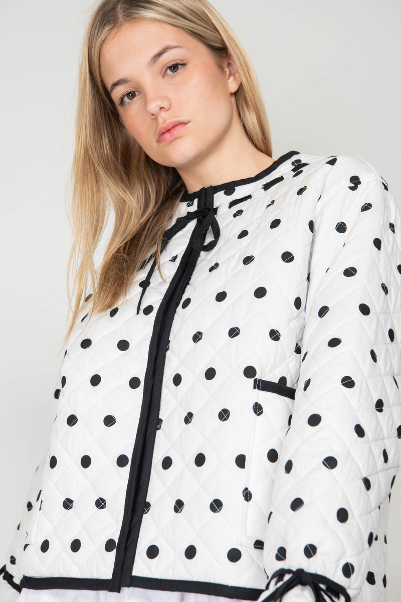 Woman wearing a black and white polka dot reversible jacket with a white skirt on a white background