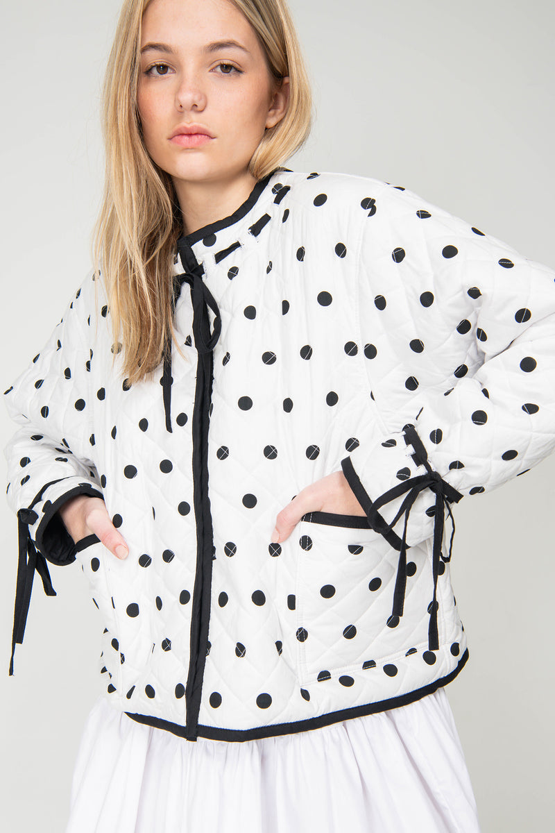 Woman wearing a black and white polka dot reversible jacket with a white skirt on a white background