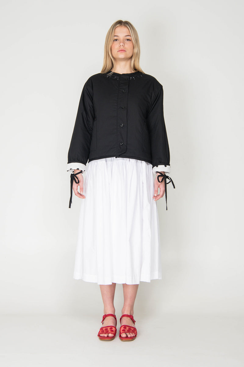Woman wearing a black and white polka dot reversible jacket with a white skirt on a white background
