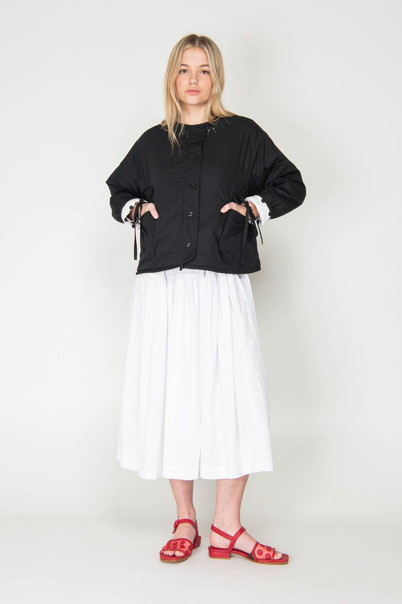 Woman wearing a black and white polka dot reversible jacket with a white skirt on a white background