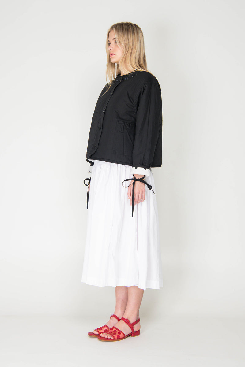 Woman wearing a black and white polka dot reversible jacket with a white skirt on a white background