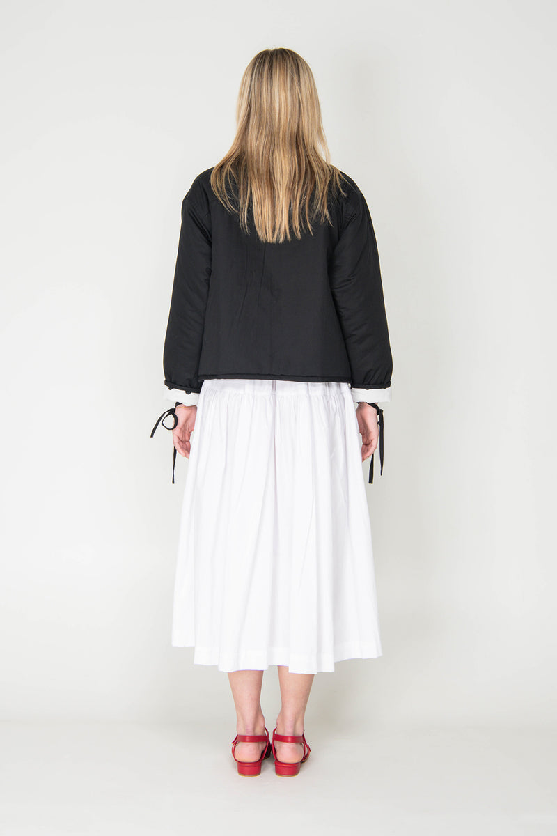 Woman wearing a black and white polka dot reversible jacket with a white skirt on a white background
