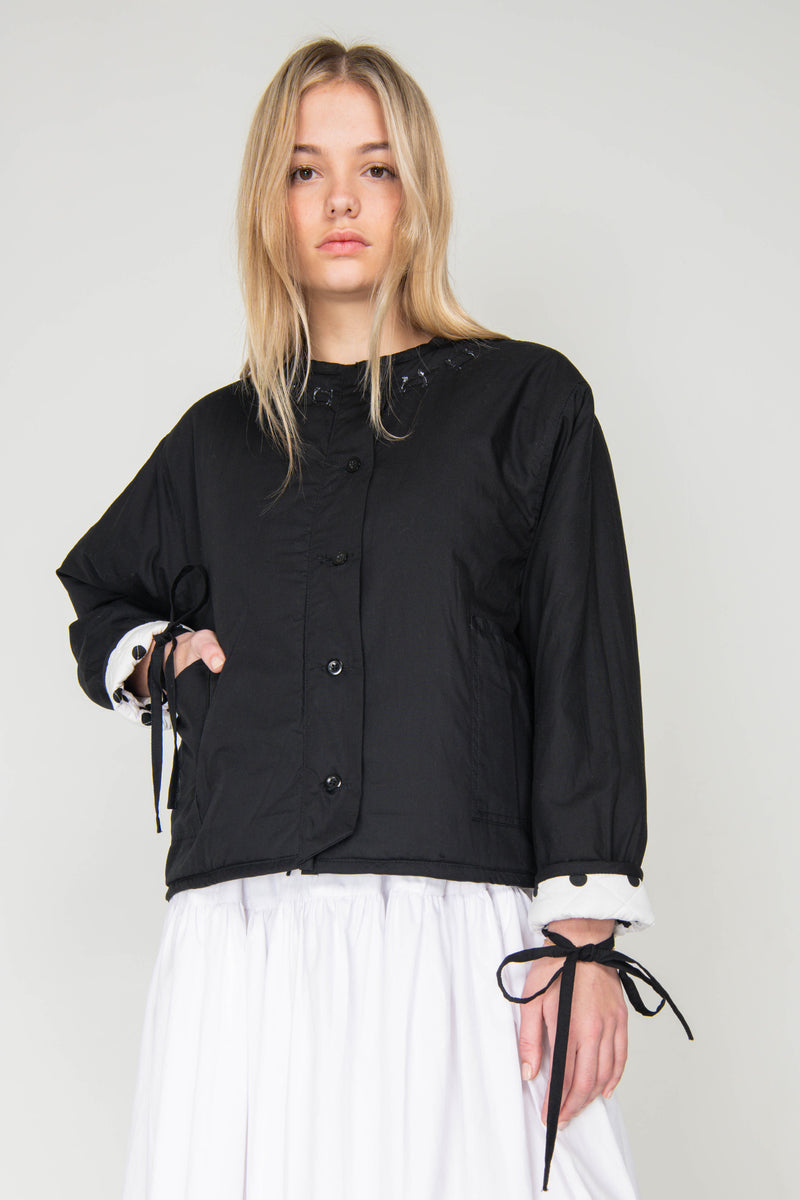 Woman wearing a black and white polka dot reversible jacket with a white skirt on a white background