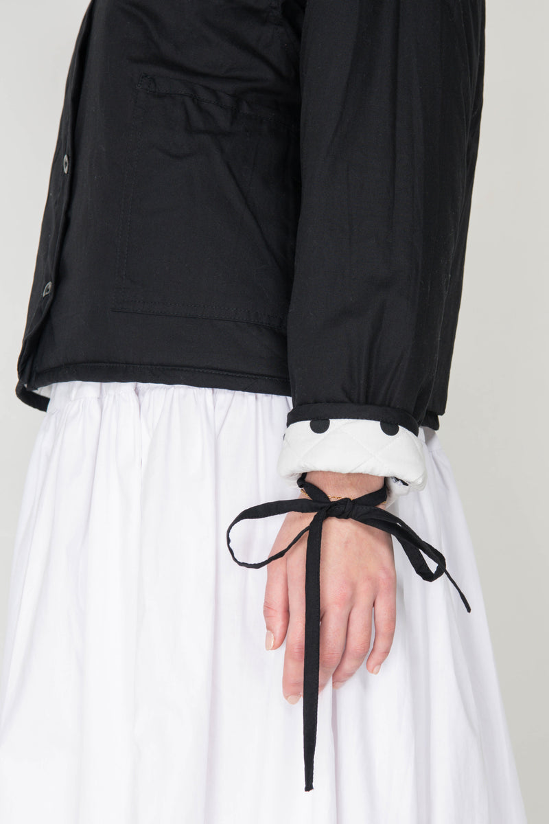 Woman wearing a black and white polka dot reversible jacket with a white skirt on a white background