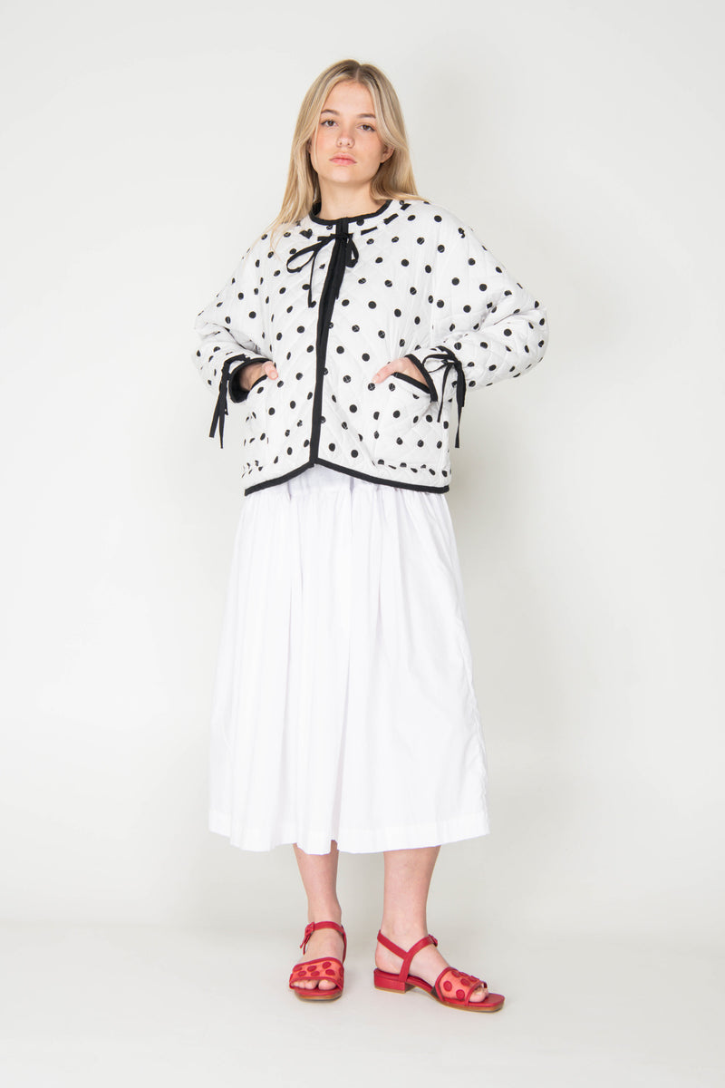 Woman wearing a black and white polka dot reversible jacket with a white skirt on a white background
