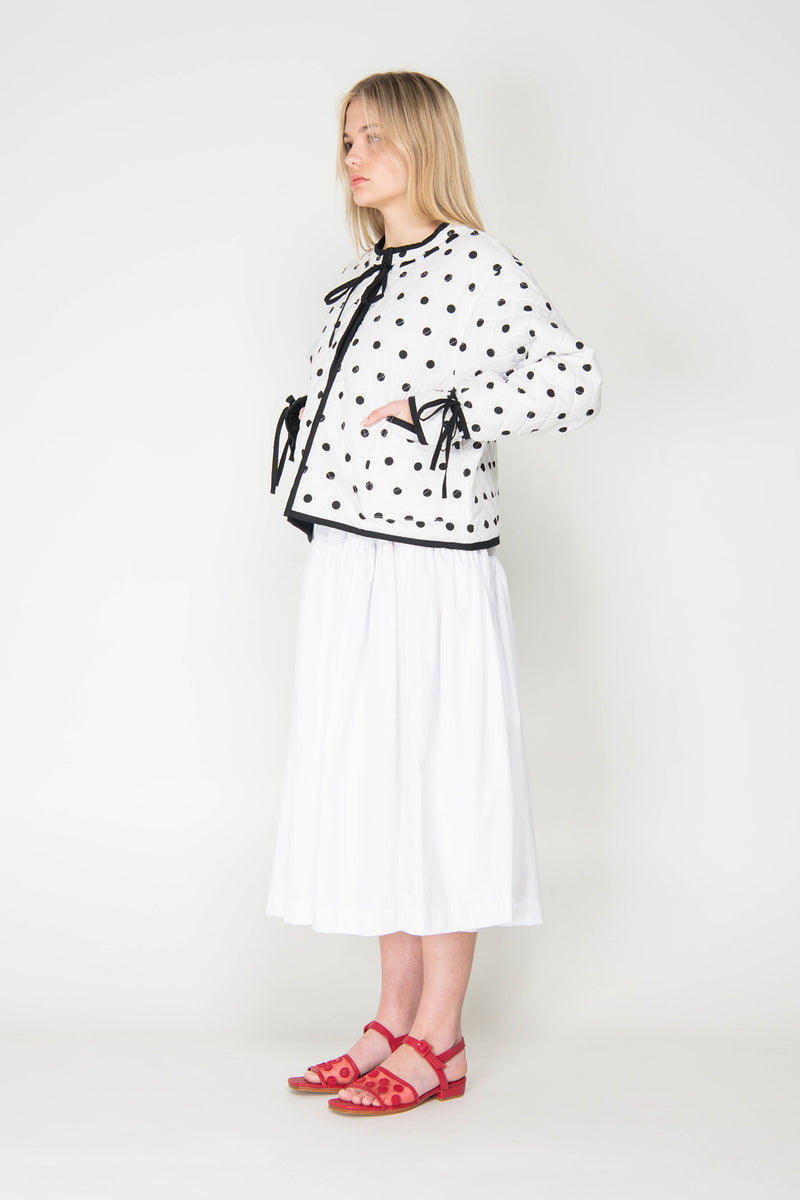 Woman wearing a black and white polka dot reversible jacket with a white skirt on a white background