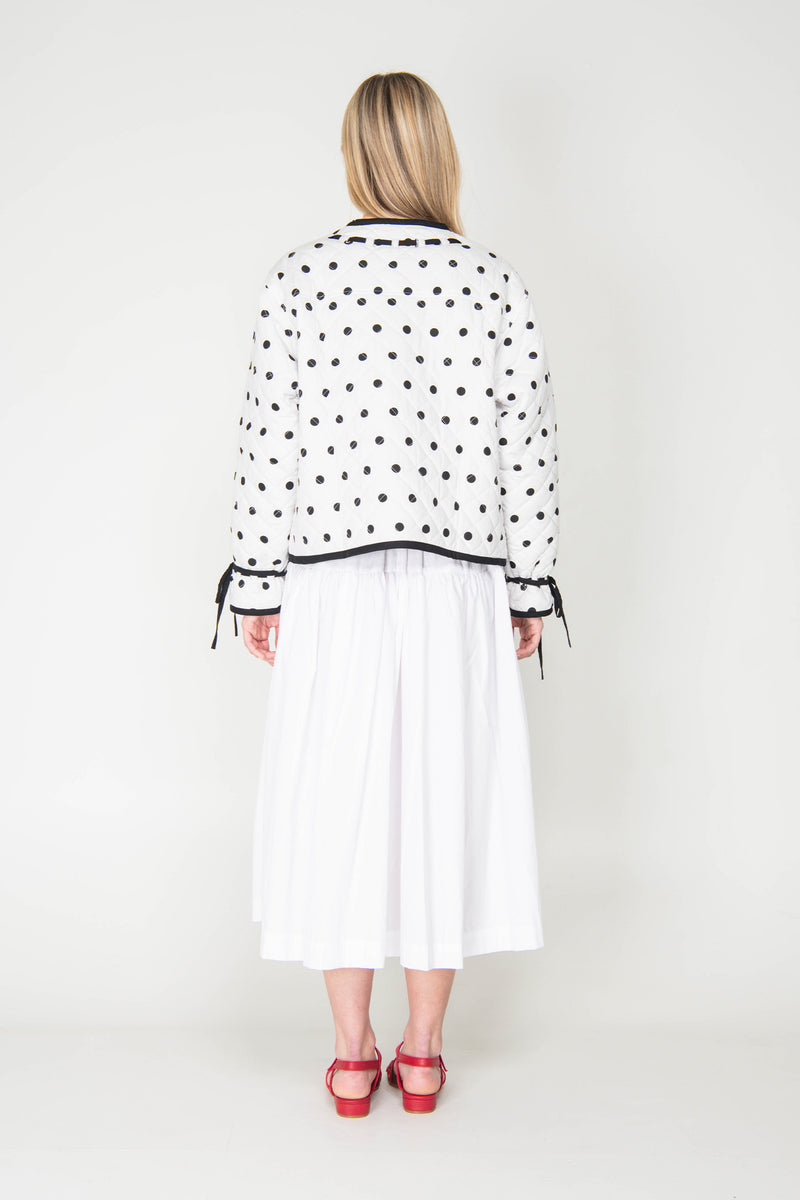 Woman wearing a black and white polka dot reversible jacket with a white skirt on a white background
