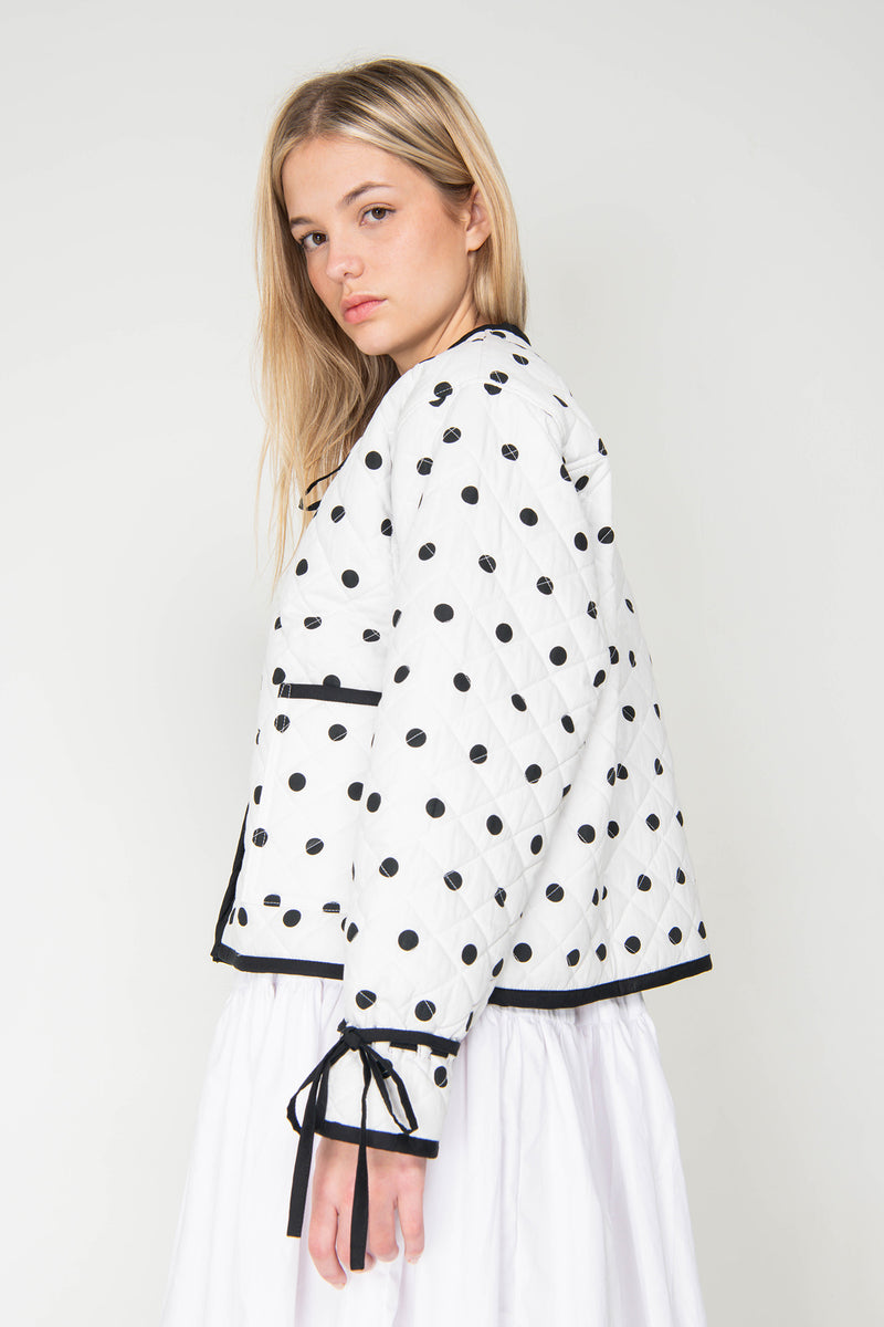 Woman wearing a black and white polka dot reversible jacket with a white skirt on a white background