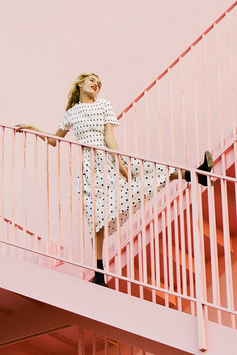 Woman in a polka dot dress standing on a pink staircase