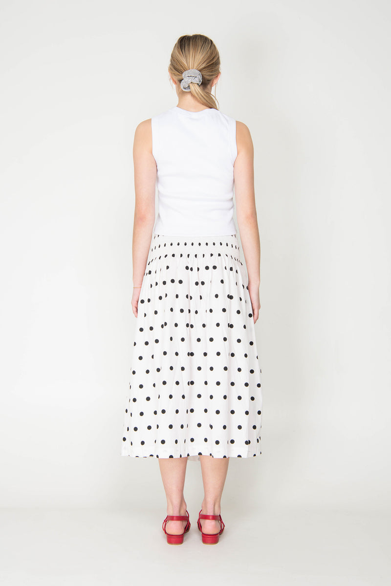 Woman wearing a white sleeveless top and polka dot skirt on a white background