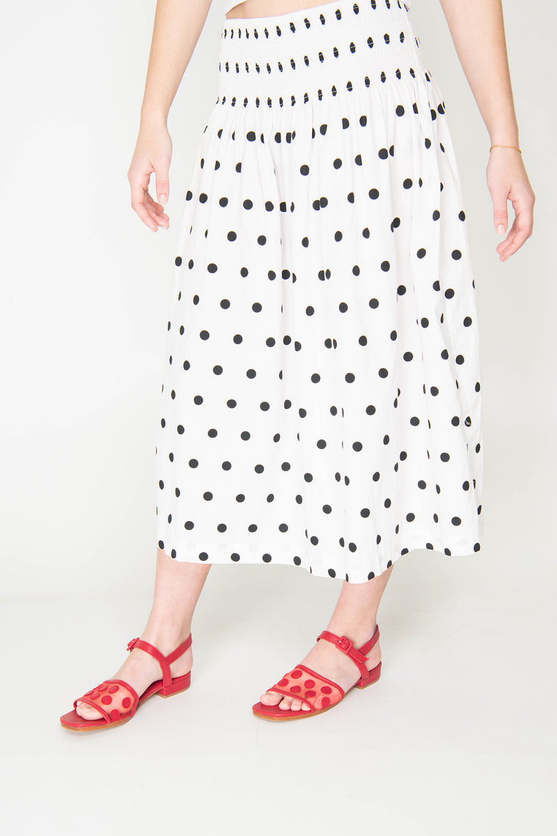 Person wearing a white skirt with black polka dots and red sandals on a white background