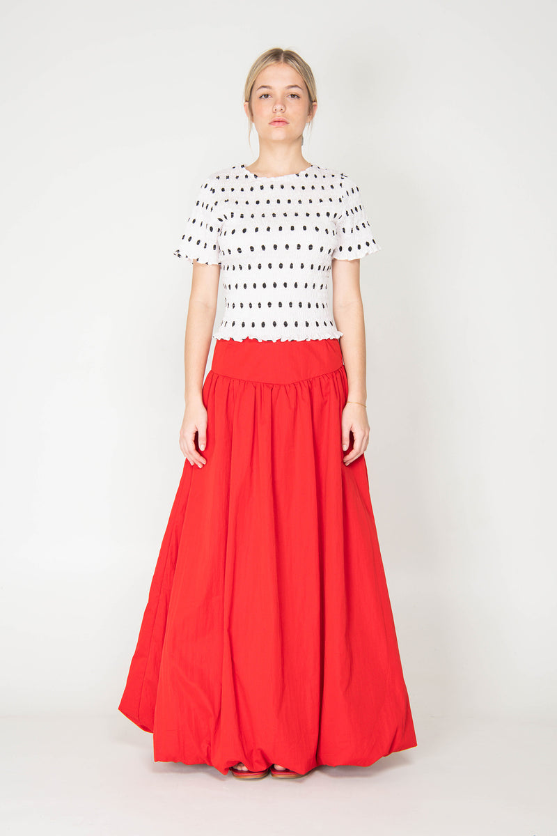 Woman wearing a white top with black polka dots and a red skirt on a white background