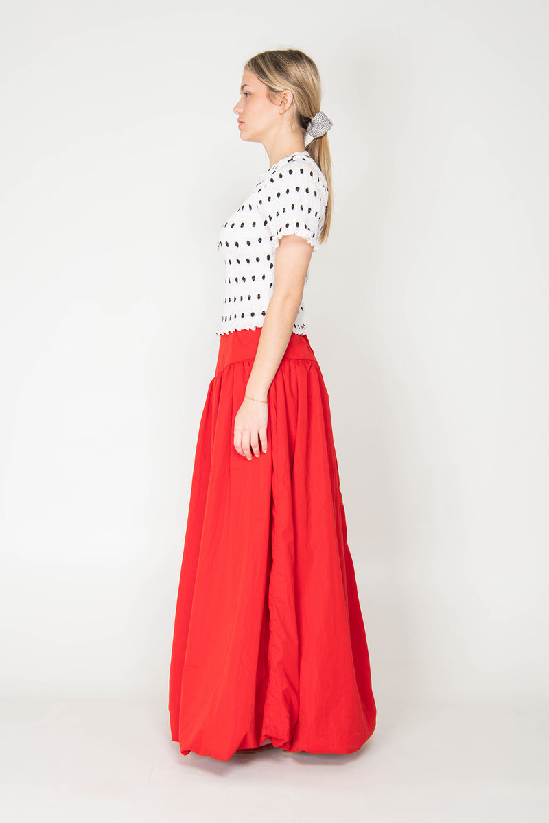 Woman wearing a white and black polka dot top with a red skirt on a white background