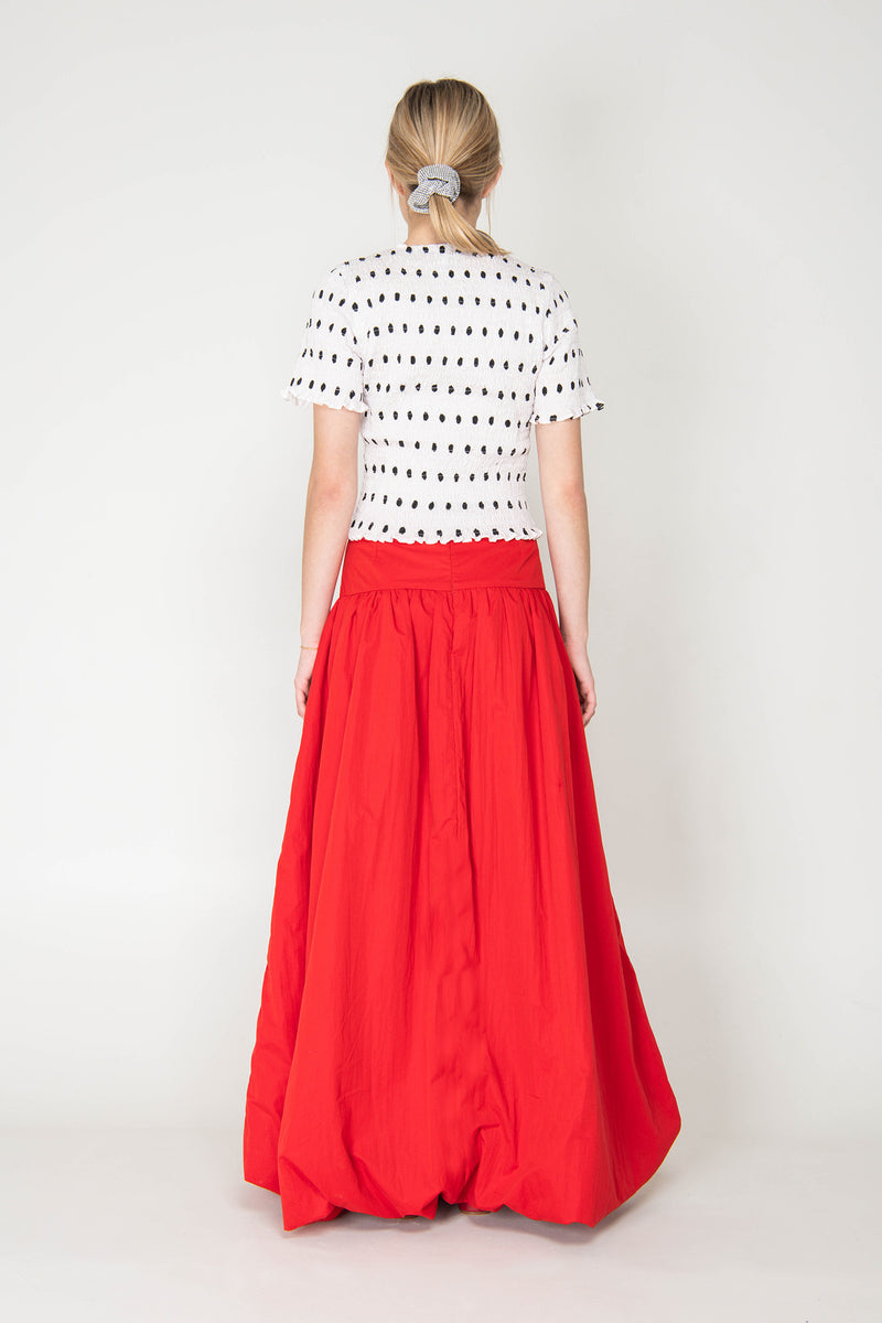 Person wearing a white blouse with black polka dots and a red skirt on a white background
