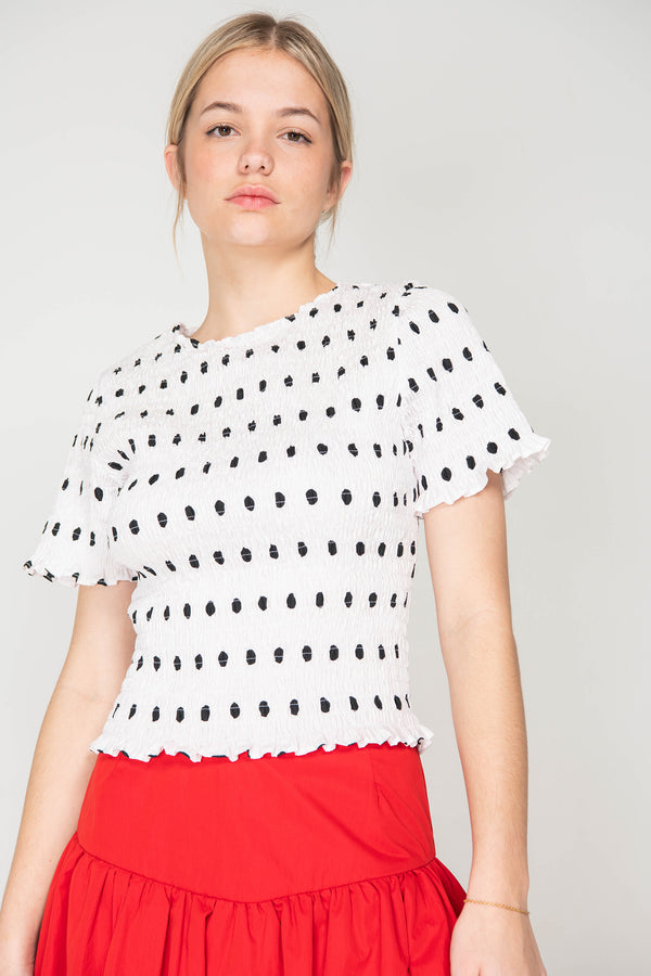 Woman wearing a white blouse with black polka dots and a red skirt on a plain background