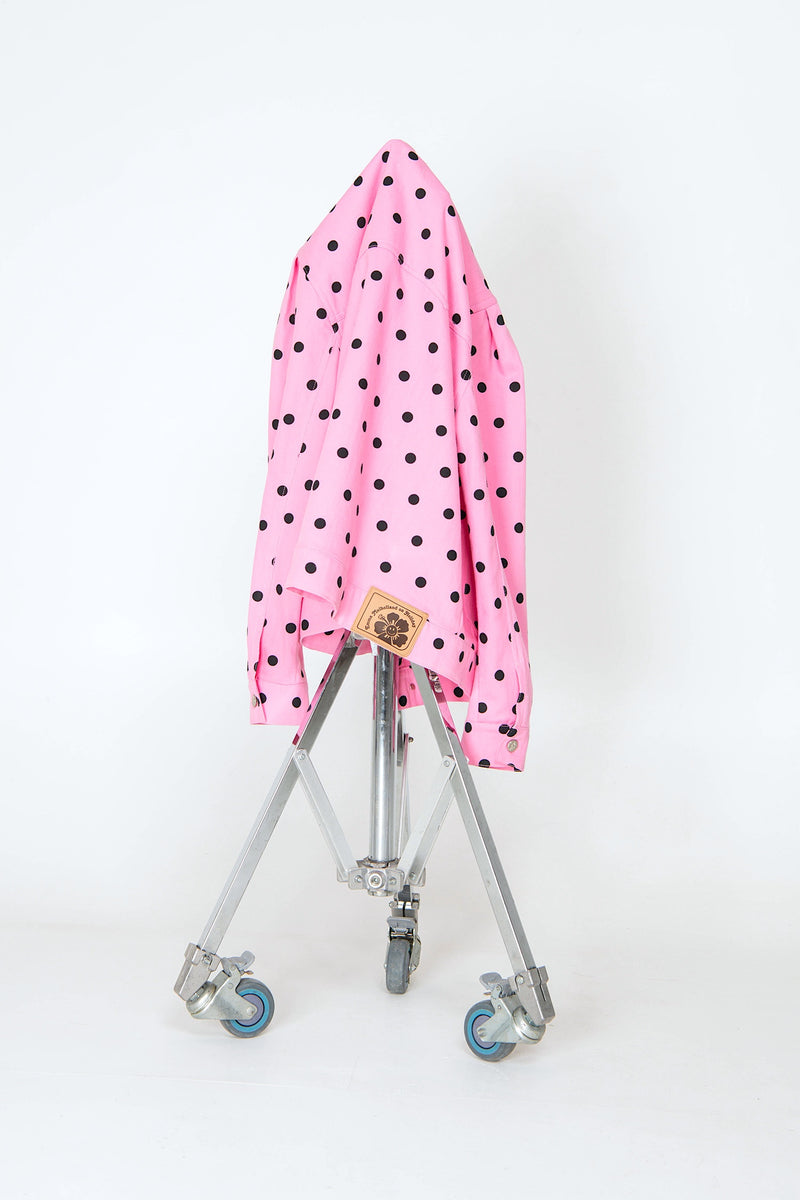 Pink umbrella with black polka dots on a metal stand against a white background