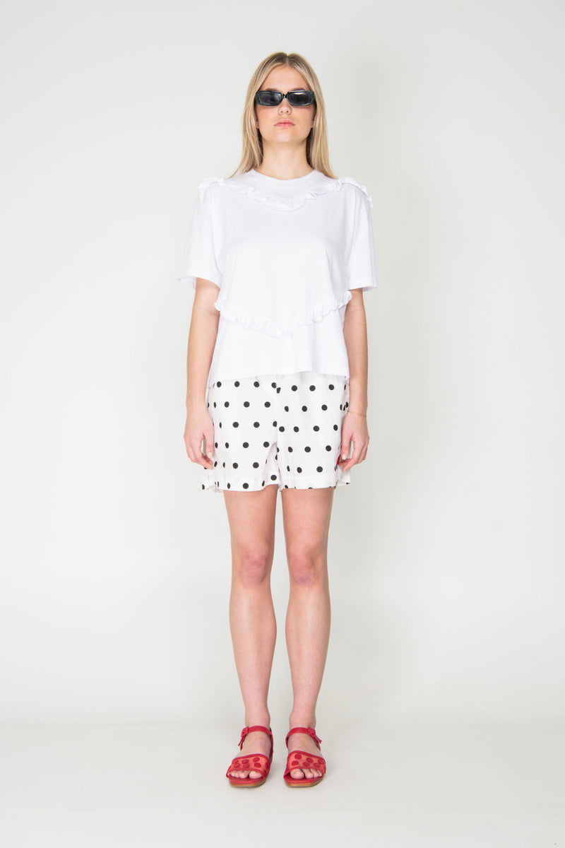 Woman wearing a white ruffled t-shirt with black polka dots and red sandals on a white background
