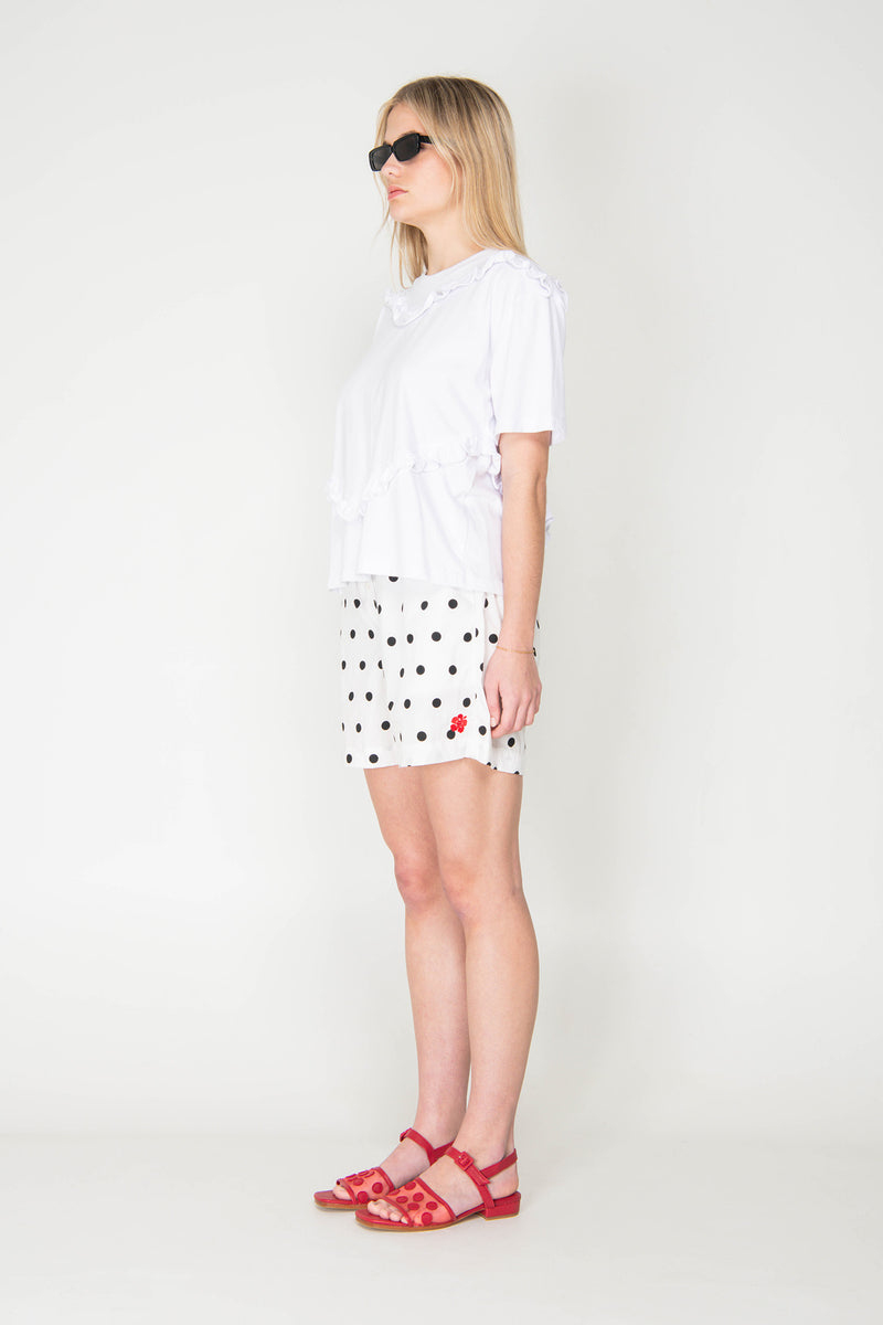 Woman wearing a white ruffled t-shirt with black polka dots and red sandals on a white background
