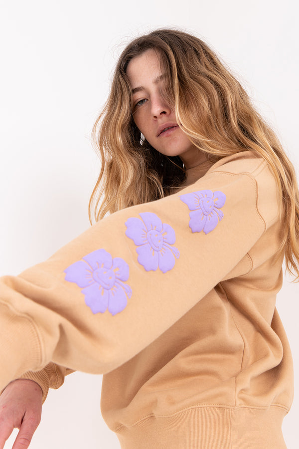 Woman wearing a beige sweatshirt with purple floral designs on a white background