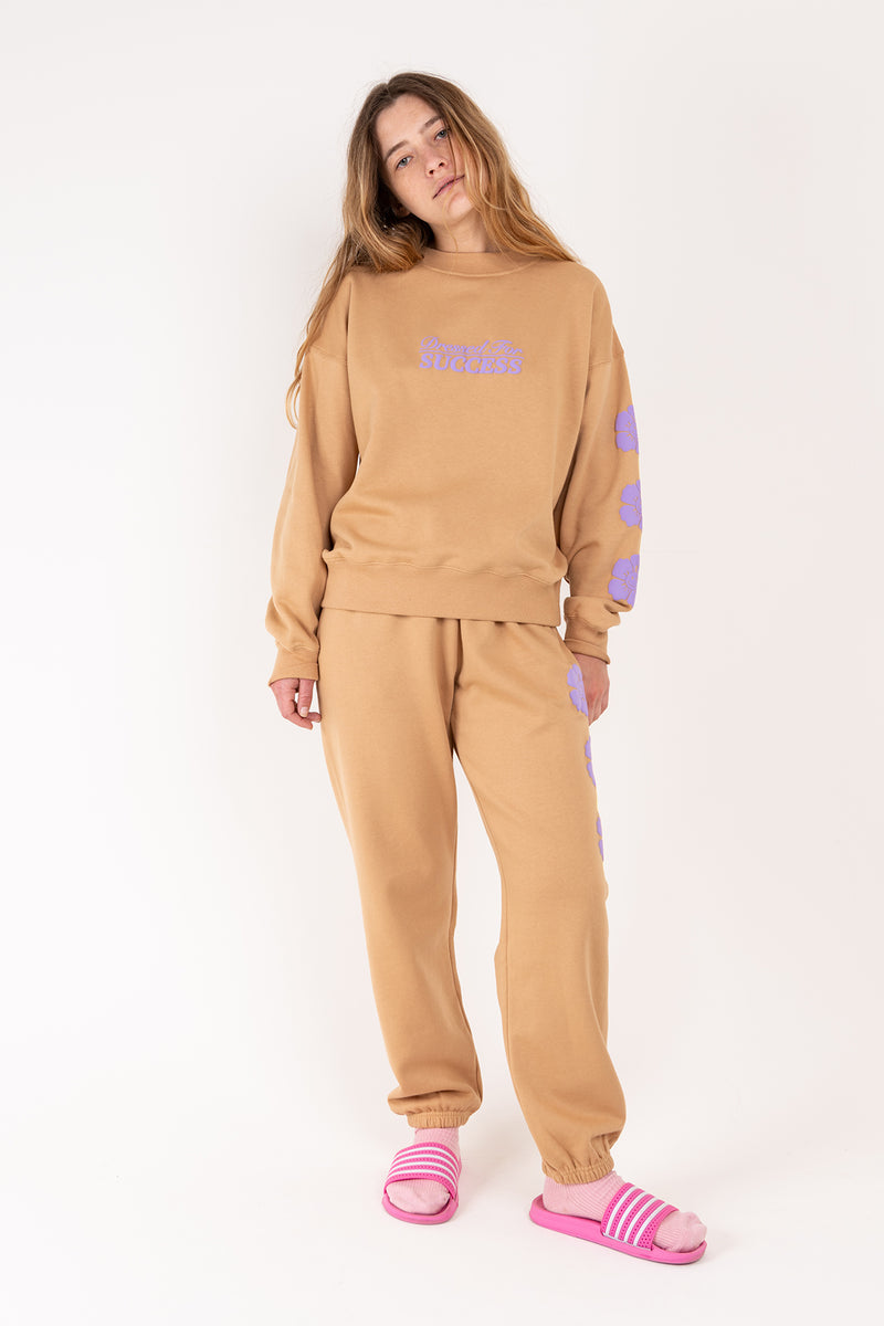 Person wearing a beige tracksuit with purple accents on a white background