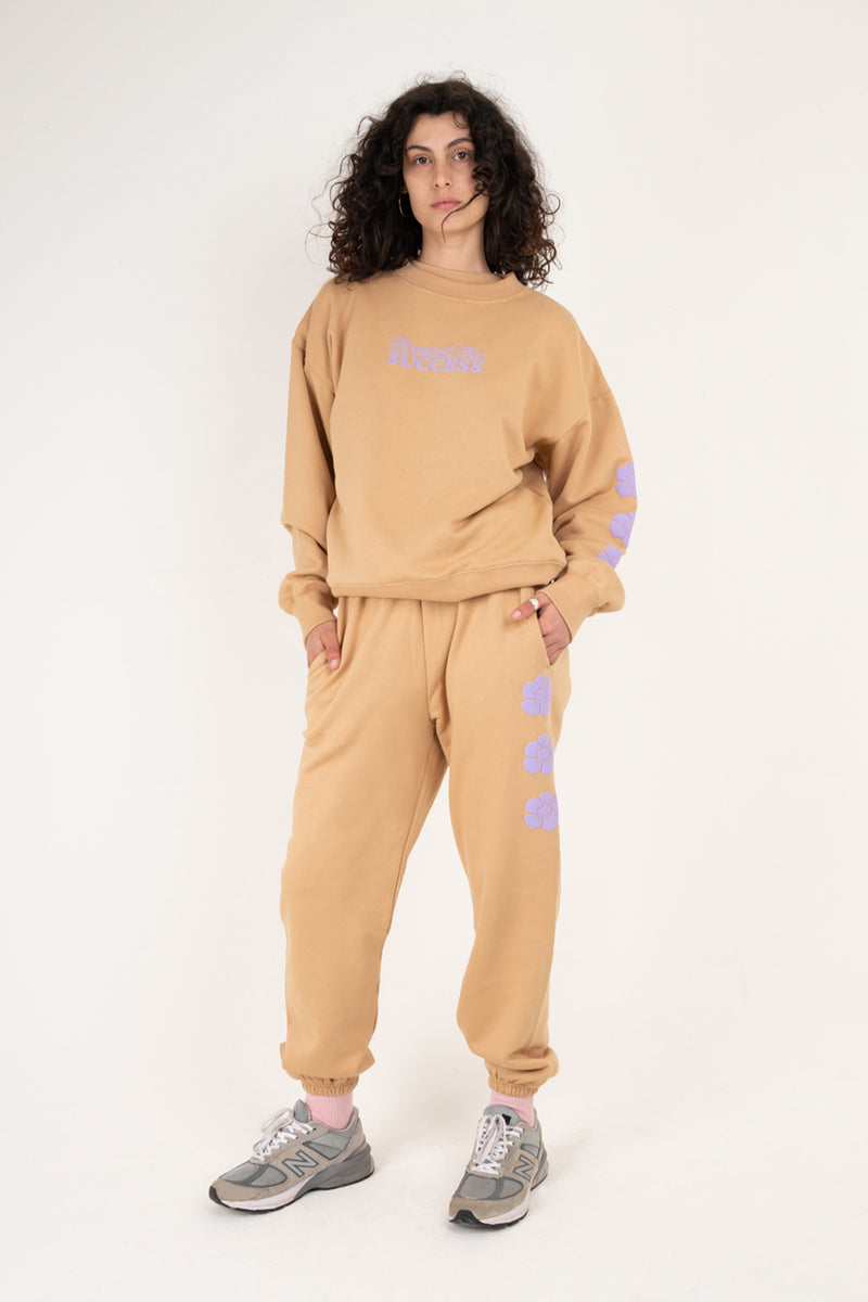 Person wearing a beige tracksuit with purple accents on a white background