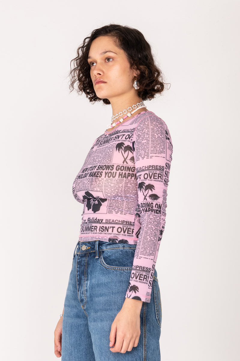 Woman wearing a patterned pink long-sleeve shirt and blue jeans on a white background