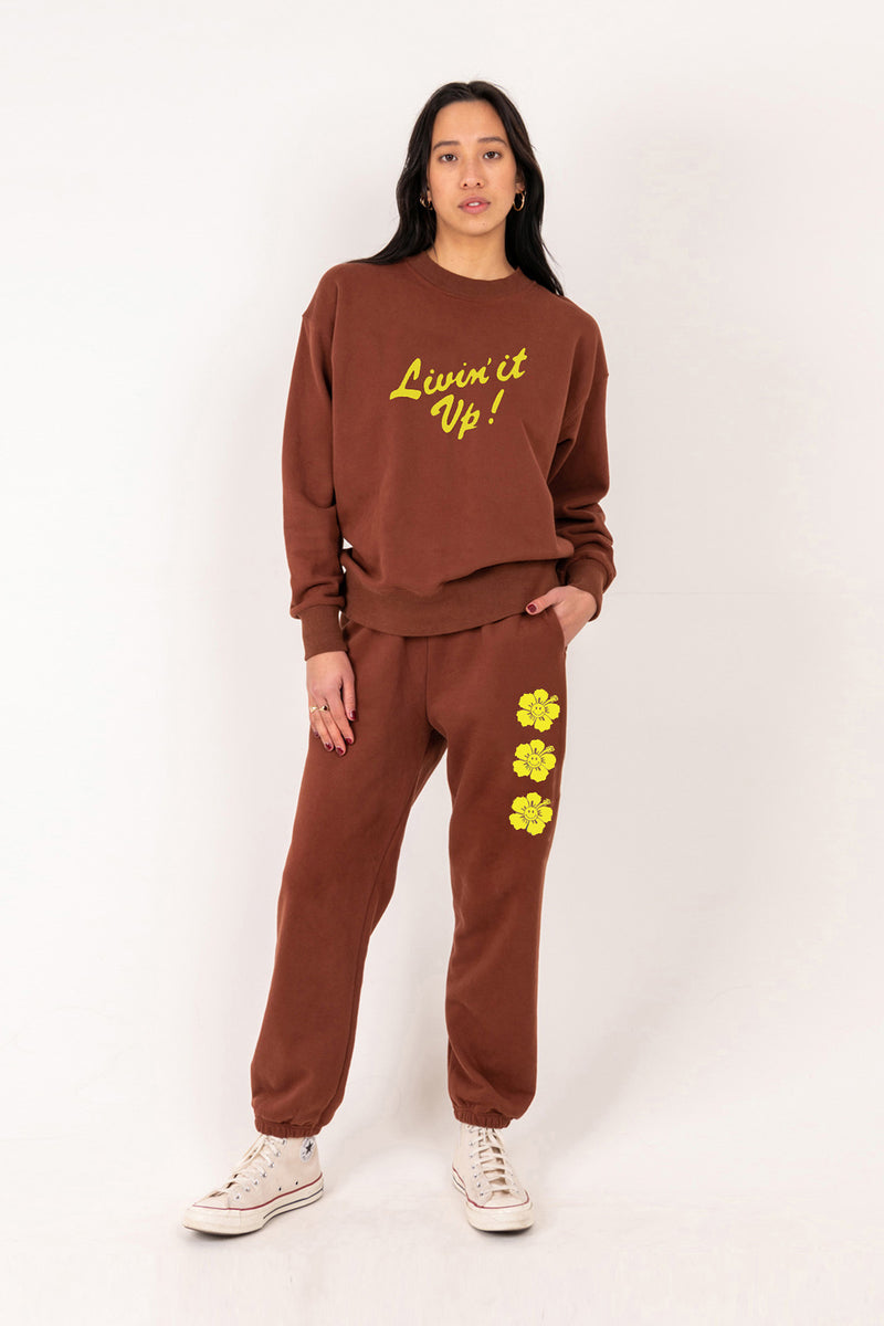 Person wearing a brown sweatshirt and pants with yellow text and flowers on a white background