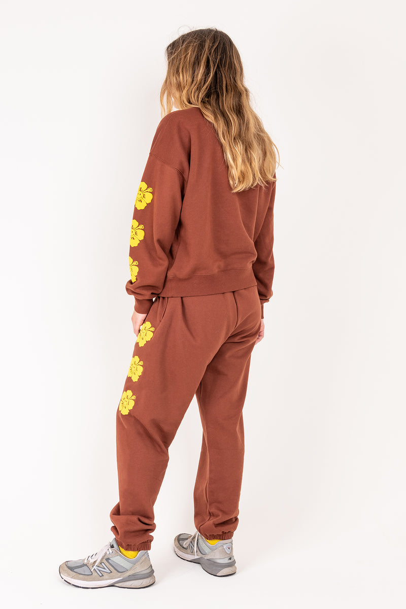 Person wearing a brown tracksuit with yellow floral patterns on a white background